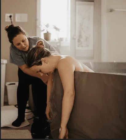 Accompagnante soutenant une femme en travail penchée sur une baignoire
